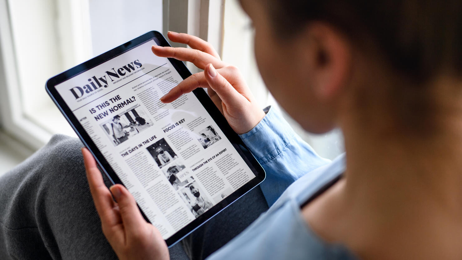 Young woman indoors at home, reading news on tablet.