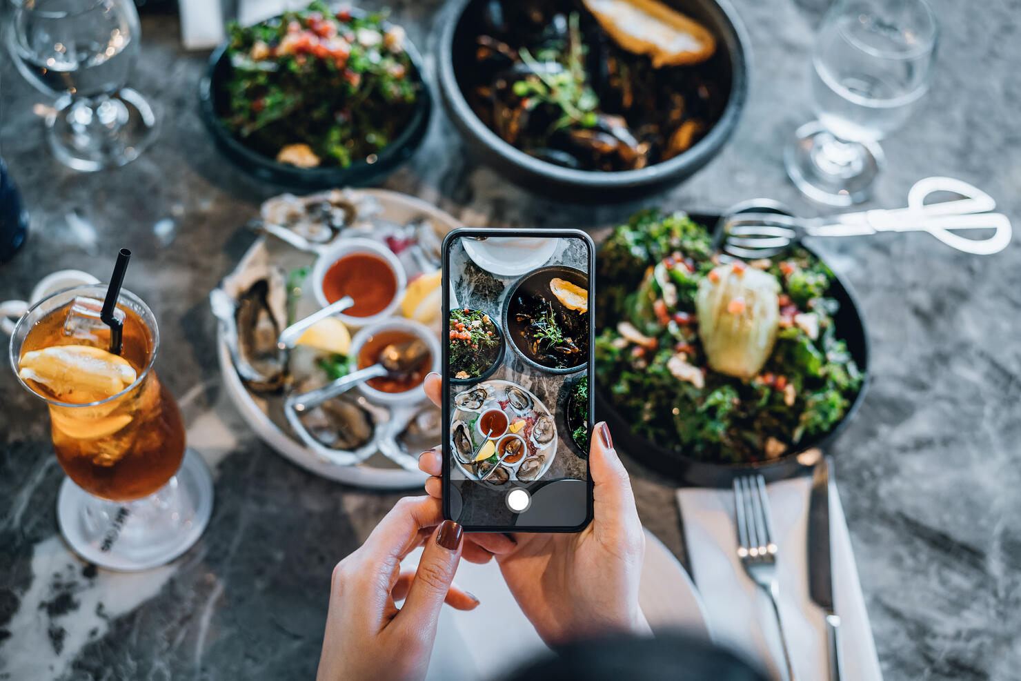 Overhead view of young woman taking photos of scrumptious and delicious meal on dining table with smartphone before eating it in restaurant. Eating out lifestyle. Camera eats first culture
