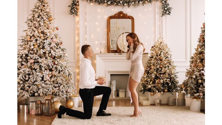 The concept of Christmas. A man makes a marriage proposal to a woman on the background of a decorated Christmas tree on a holiday in a luxury house in winter. A couple in love in elegant outfits celebrates the holiday together