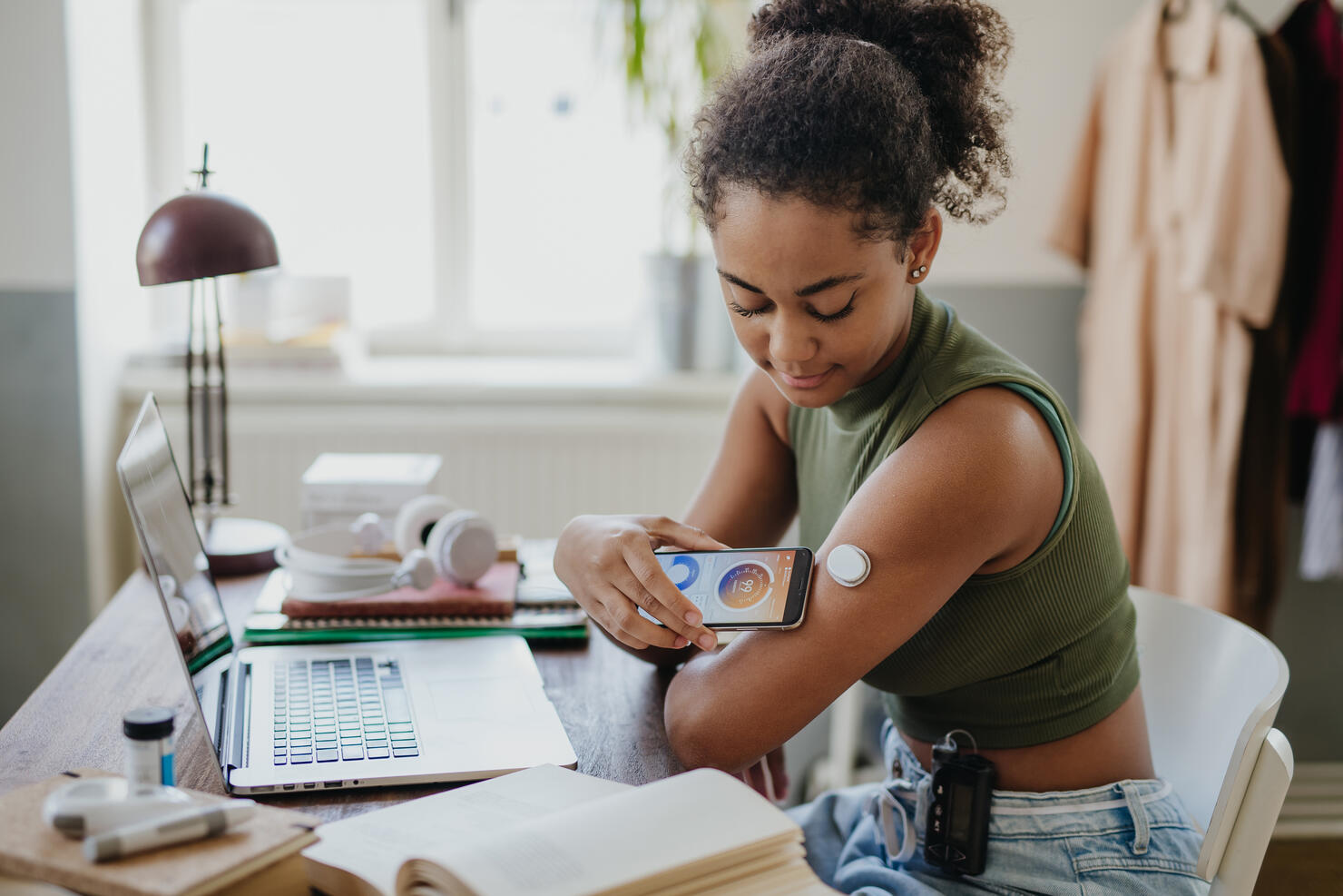 Teenage girl connecting smartphone to continuous glucose monitor, checking blood glucose during day. Student doing routine blood check while studying.