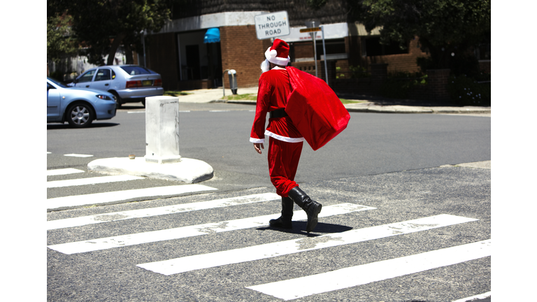 Man dressed as Santa Claus carrying sack walking across street, rear view