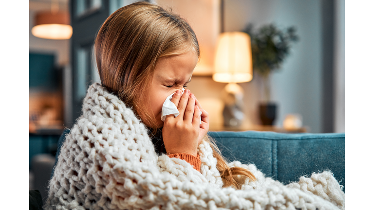 Season of flu. Little kid covered with blanket pressing handkerchief to nose while sneezing at apartment