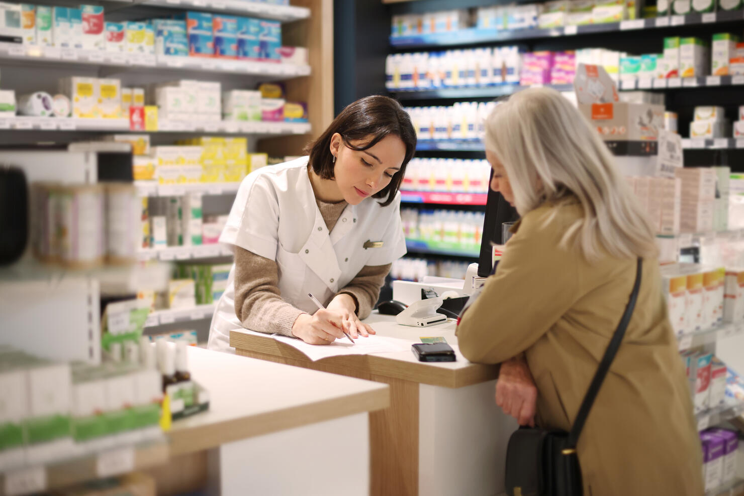 A female pharmacist discussing a prescription with an elderly lady customer at the service counter in a pharmacy.