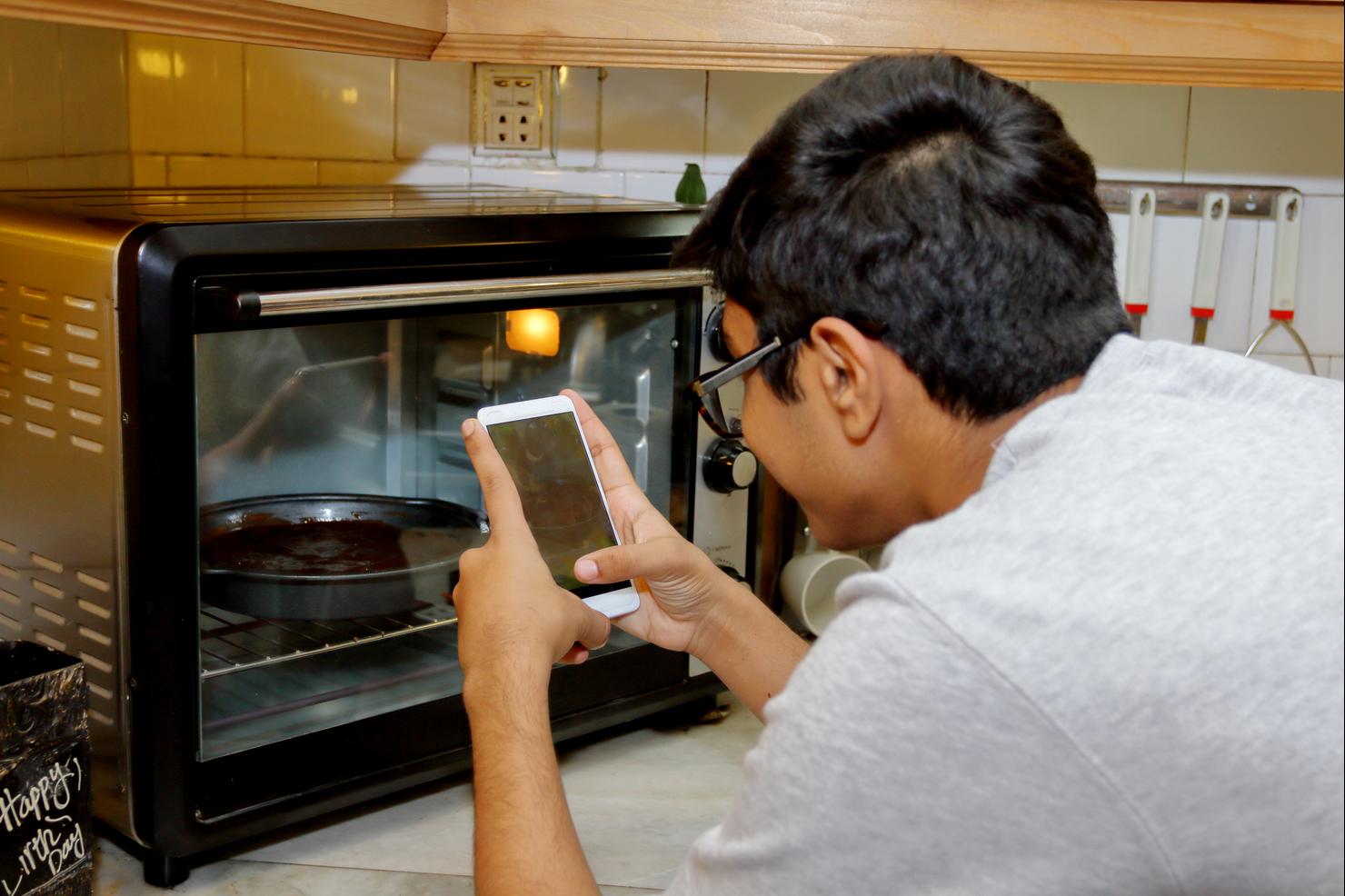 A teenager boy taking photo with mobile phone camera of a baking brownie in the oven