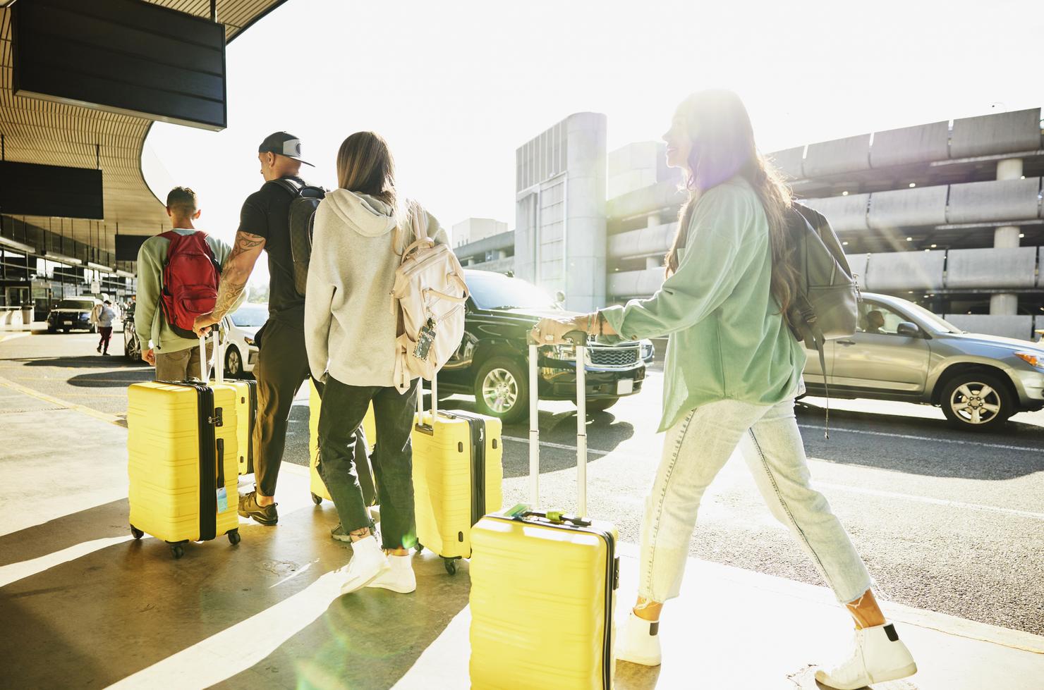 Wide shot of family walking luggage into airport before flight