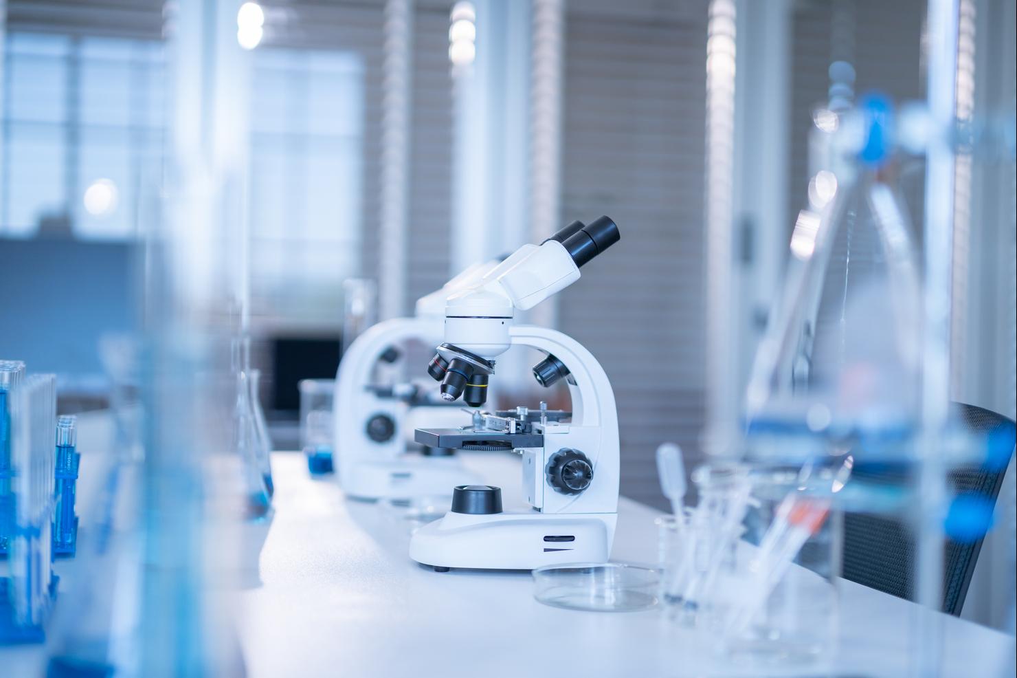 Microscope and test tubes row with light blue liquid at science laboratory
