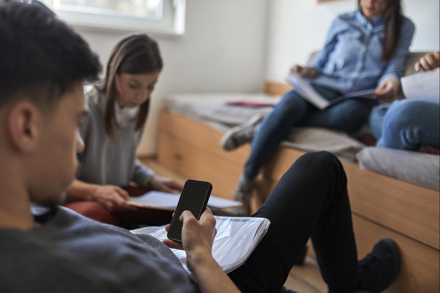 Student in dormitory using smartphone with fellow students in background