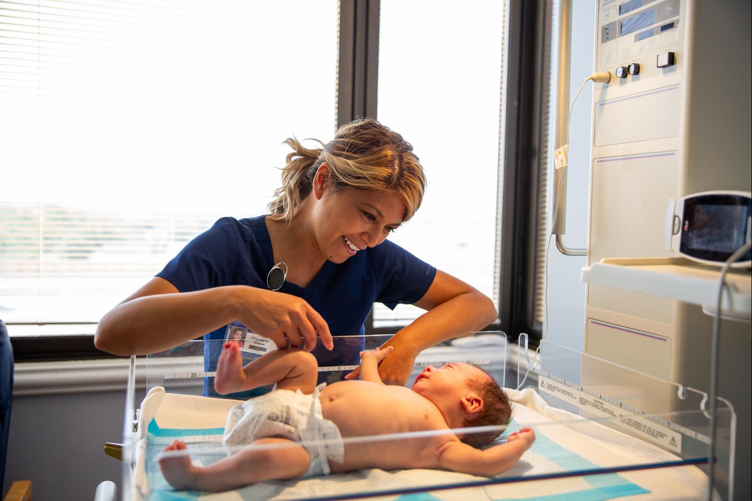 Lead nurse smiling at a newborn baby boy laying in the incubator in a hospital room.