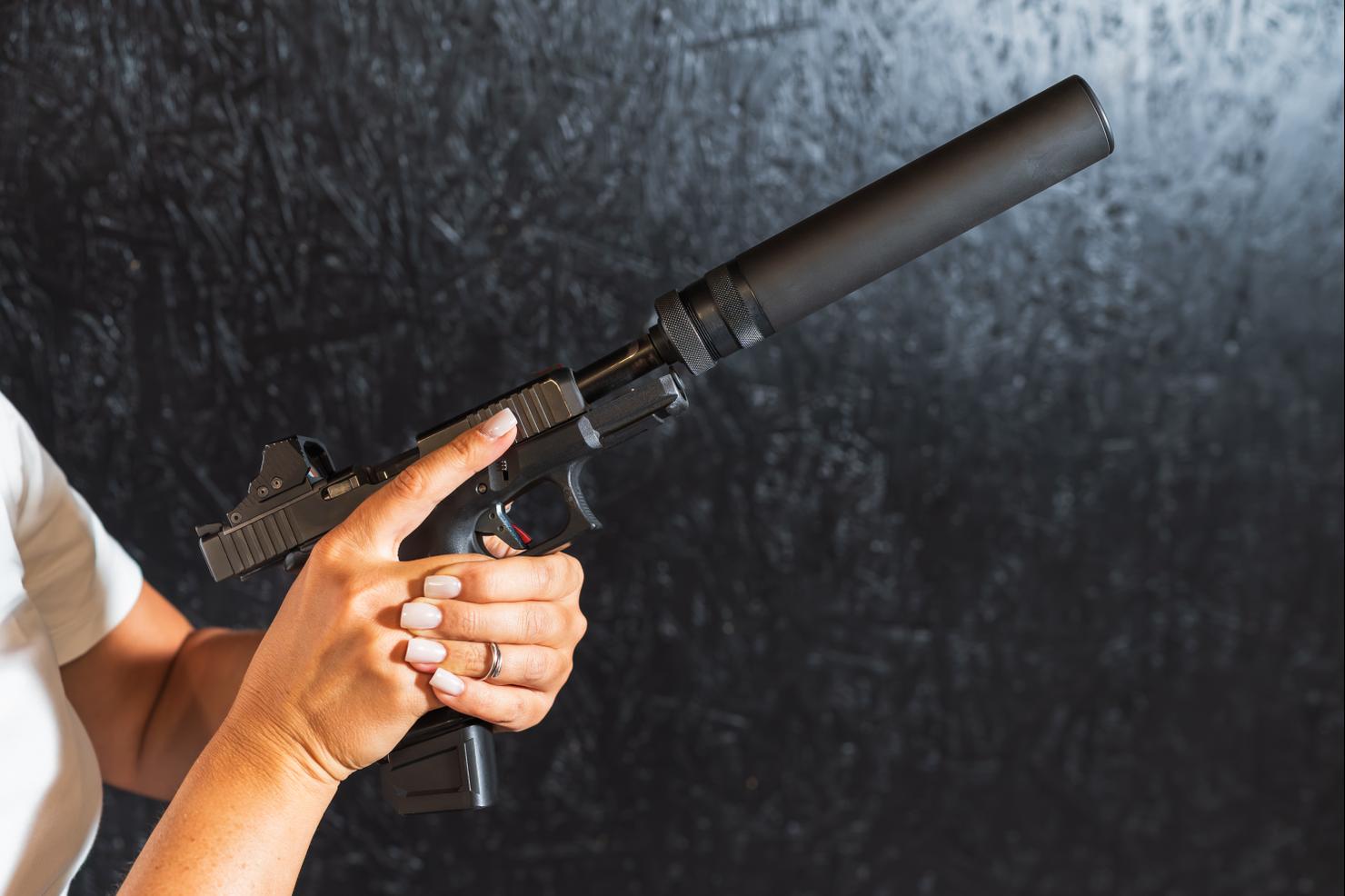 A woman's hands with a manicure holding a modern handgun equipped with a silencer and red dot sight.