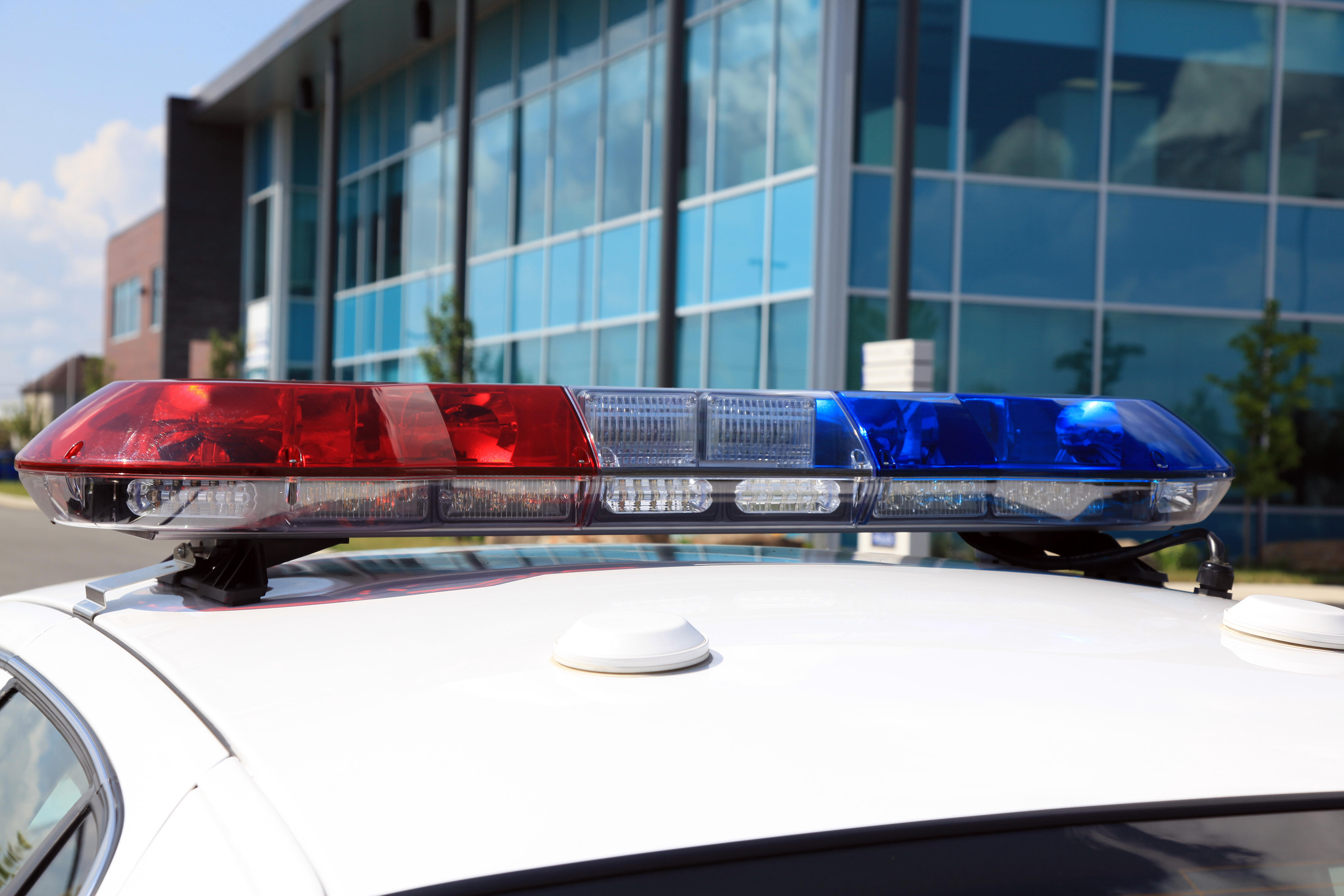 DSLR picture of a modern police car light bar equipment on top of a white police car. In the background there is a modern glass building.