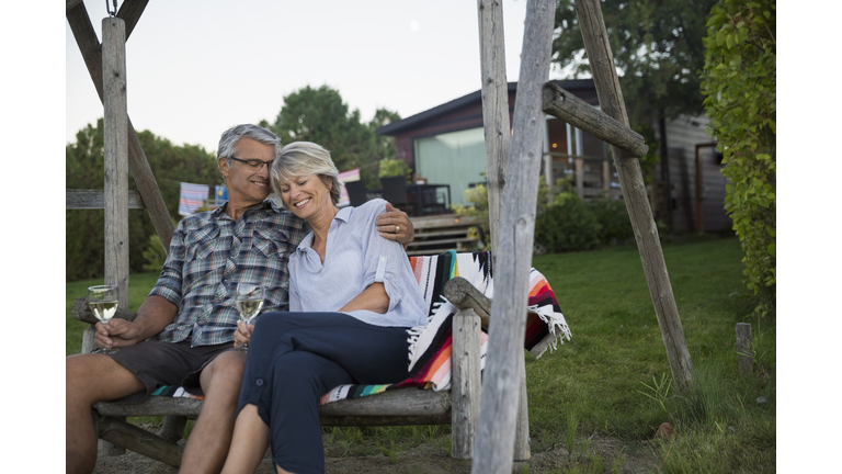 Serene retired couple drinking white wine on lake house swing