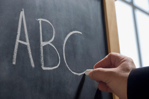 Hispanic teacher writing 'ABC' on chalkboard