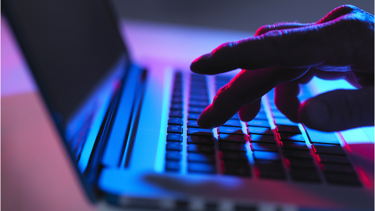 Silhouette of male hand typing on laptop keyboard at night