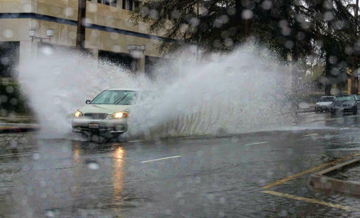 A car drives through a flooded street in the Van Nuys section of Los Angeles on Sunday, Jan. 22, 2017. California residents evacuated neighborhoods below hillsides scarred by wildfires as the third, and largest, in the latest series of storms brought powe