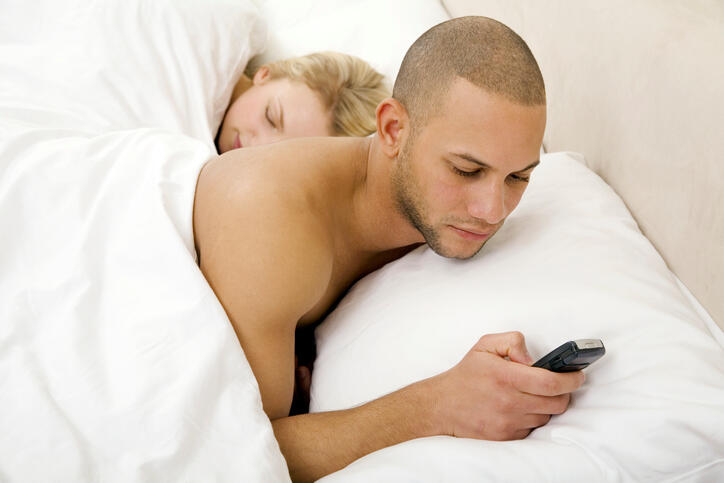 Young man text messaging with young woman sleeping
