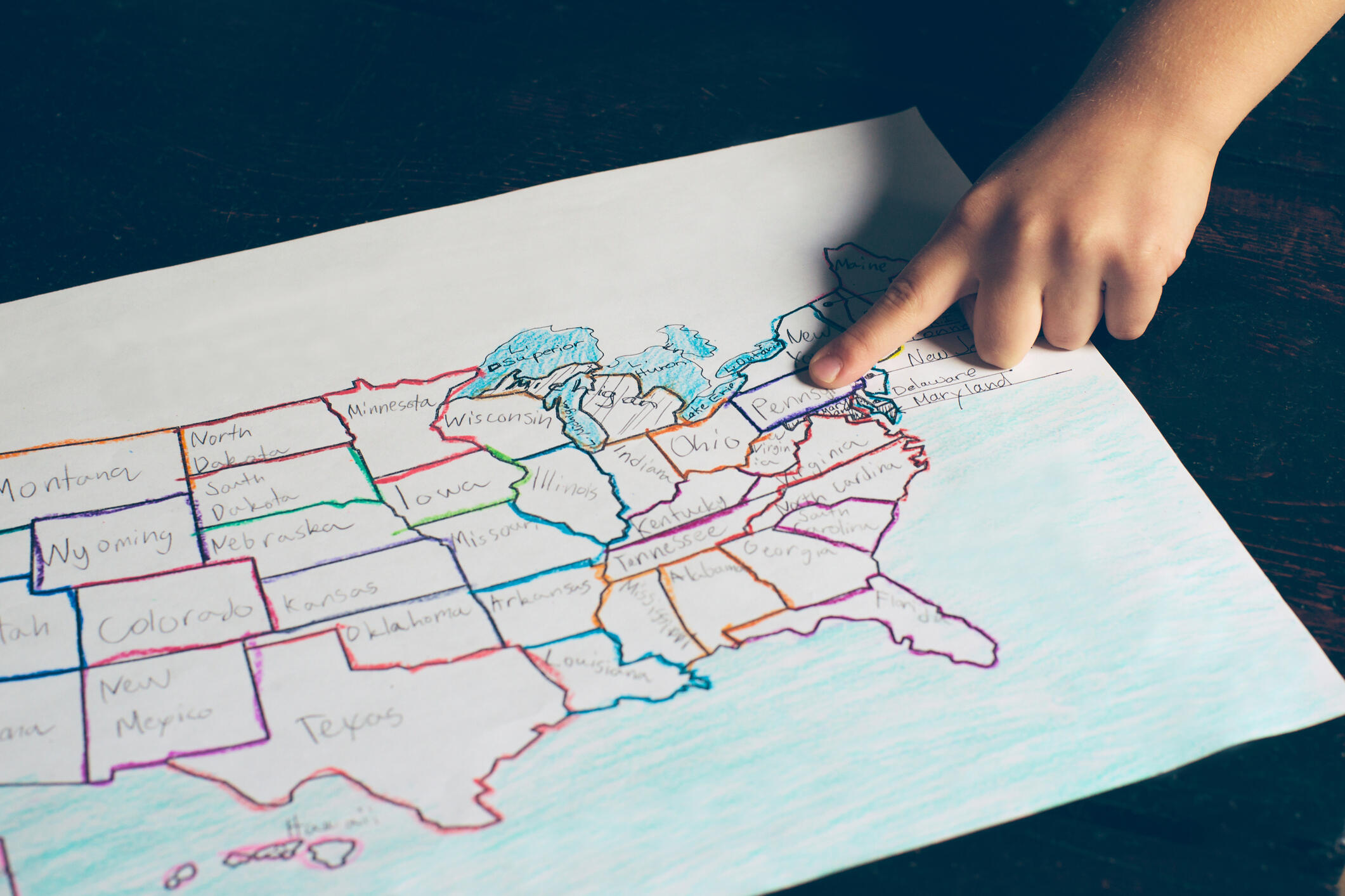 A child's finger pointing to a hand drawn map of the United States of America.