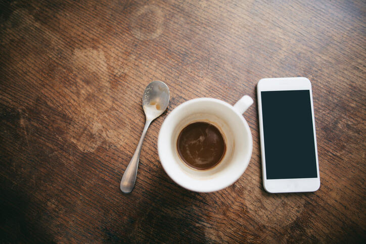 Coffee cup with remains of coffee, spoon and smartphone on wood