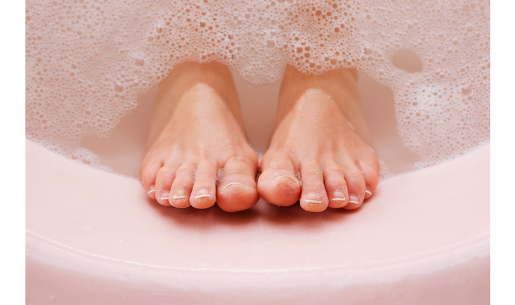 woman's feet resting against bath tub with bubbles