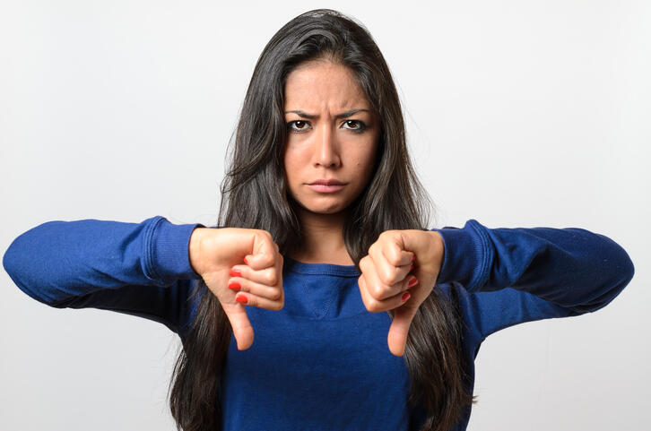 Portrait Of Young Woman Gesturing Thumbs Down Against White Background