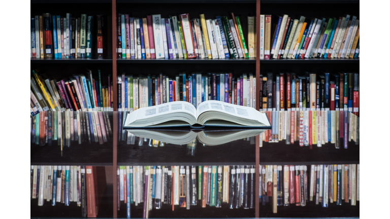 An open book on table front of shelves filled with books