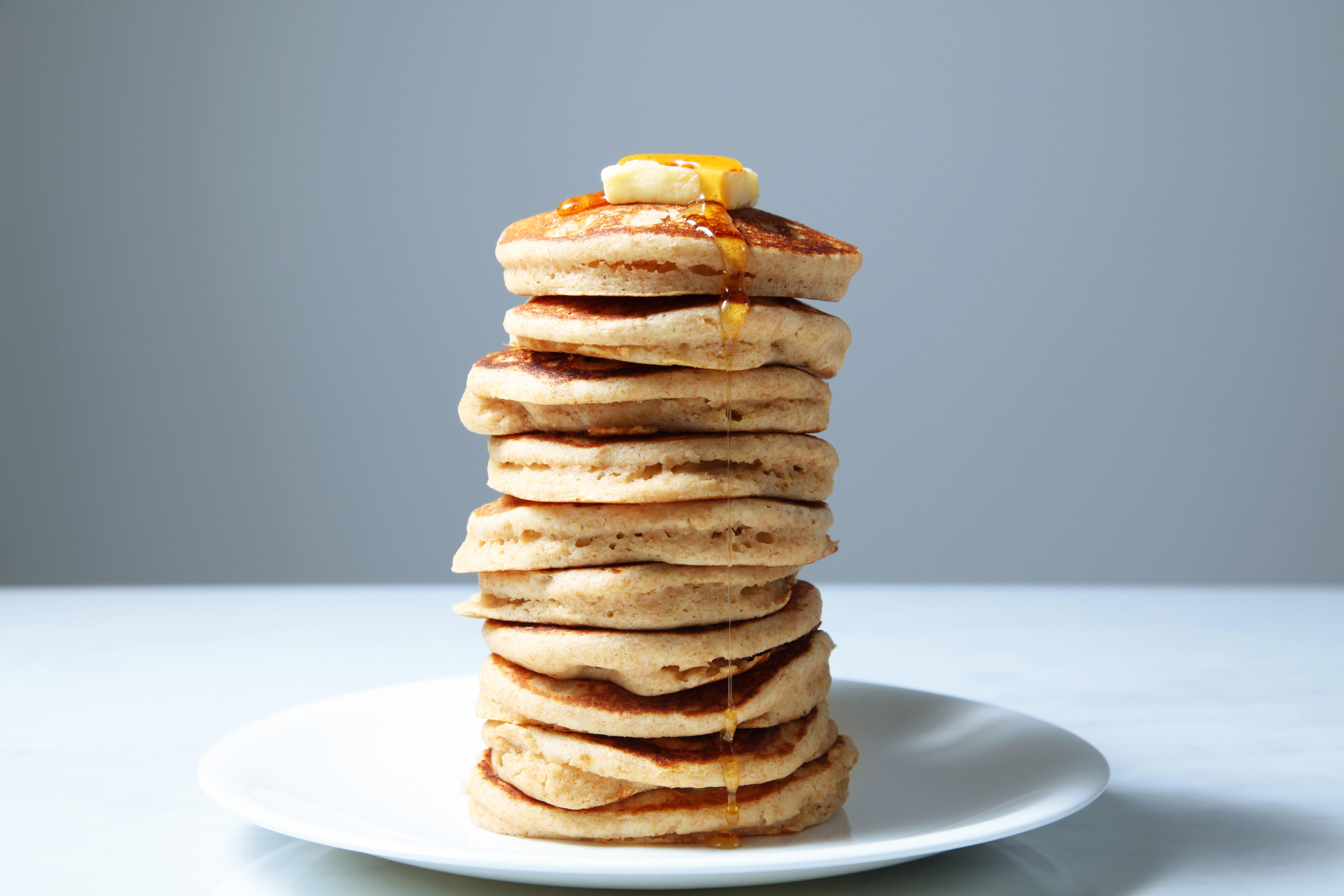 A large stack of fluffy wheat pancakes on a white plate.  golden yellow butter and maple syrup.   