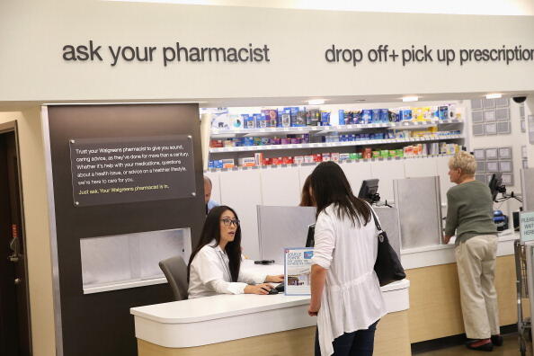 WHEELING, IL - SEPTEMBER 19:  Pharmacist Jeanie Kim (L) consults with a customer at a Walgreens pharmacy on September 19, 2013 in Wheeling, Illinois. Walgreens, the nation's largest drugstore chain, yesterday disclosed a plan to provide payments to roughl