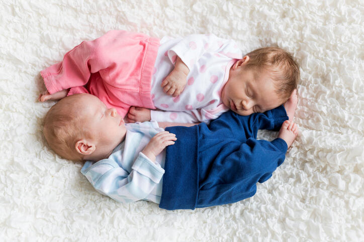 Newborn twins sleeping on white blanket