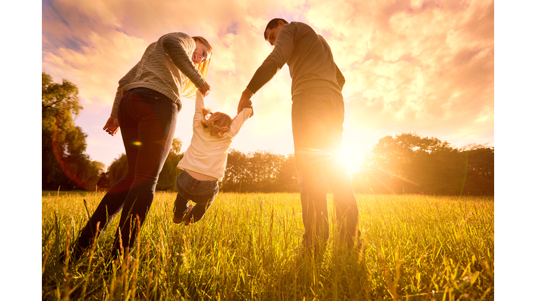 Parents hold baby's hands.  Happy family in park evening