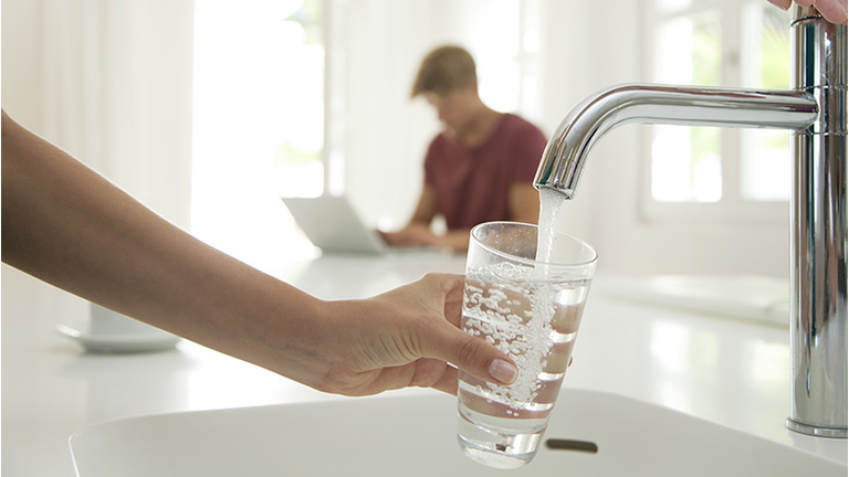 Woman filling glass of water at kitchen sink, cropped