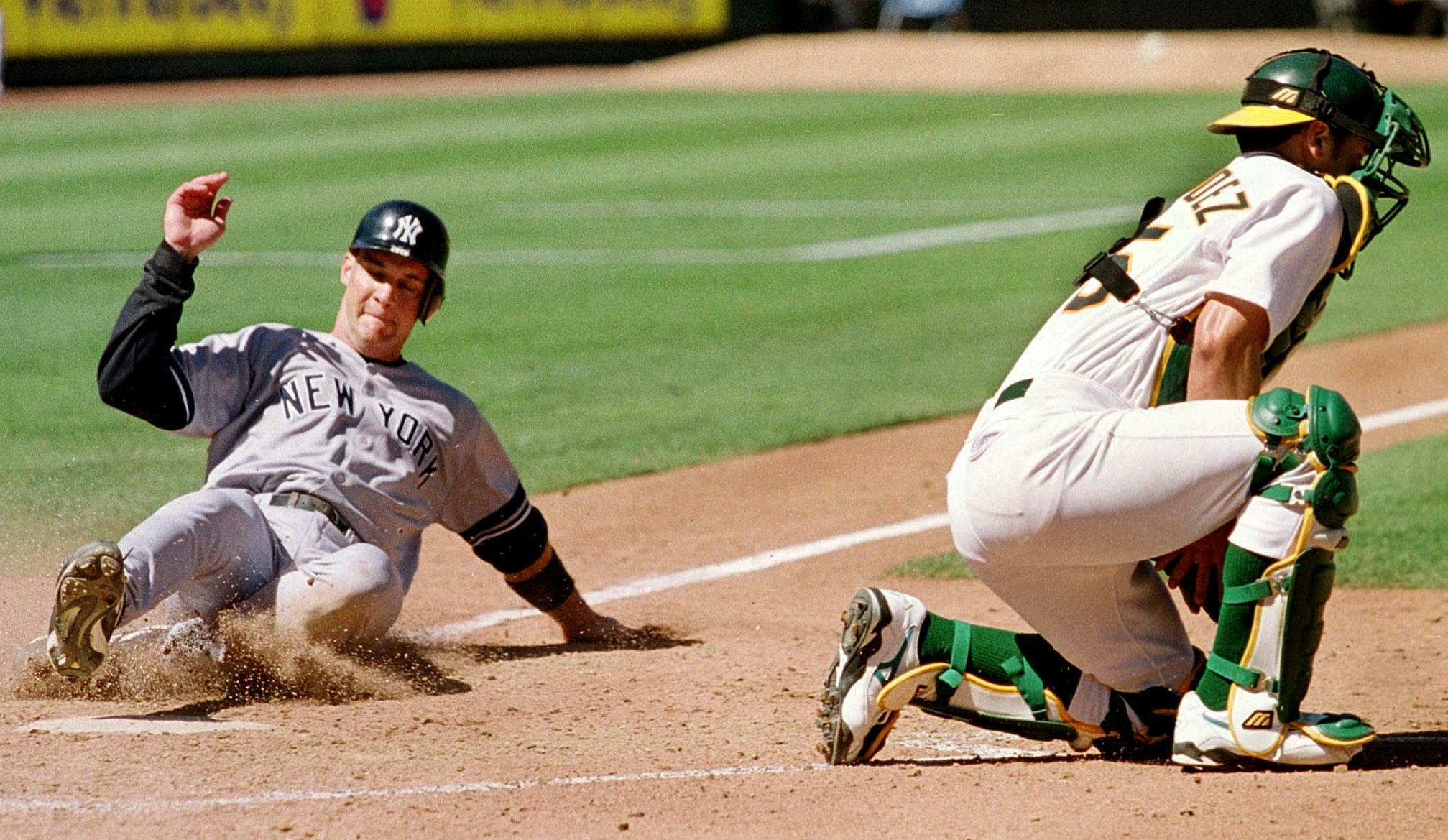 OAKLAND, UNITED STATES:  New York Yankees Clay Bellinger (L) slides safely into home plate, beating the tag from Oakland Athletics catcher Ramon Hernandez (R) during the fifth inning in Oakland, California, 26 August 2000. The Yankees defeated the A's 10-