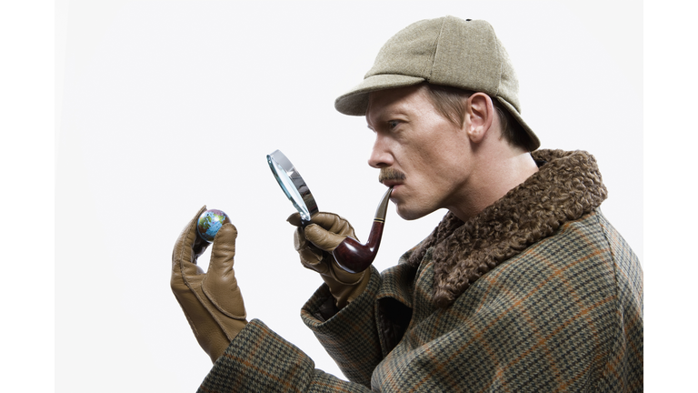 A man dressed up as Sherlock Holmes looking at a tiny globe through a magnifying glass
