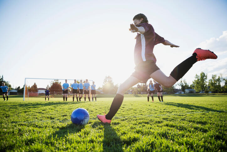 Middle school girl soccer player kicking free kick on sunny field