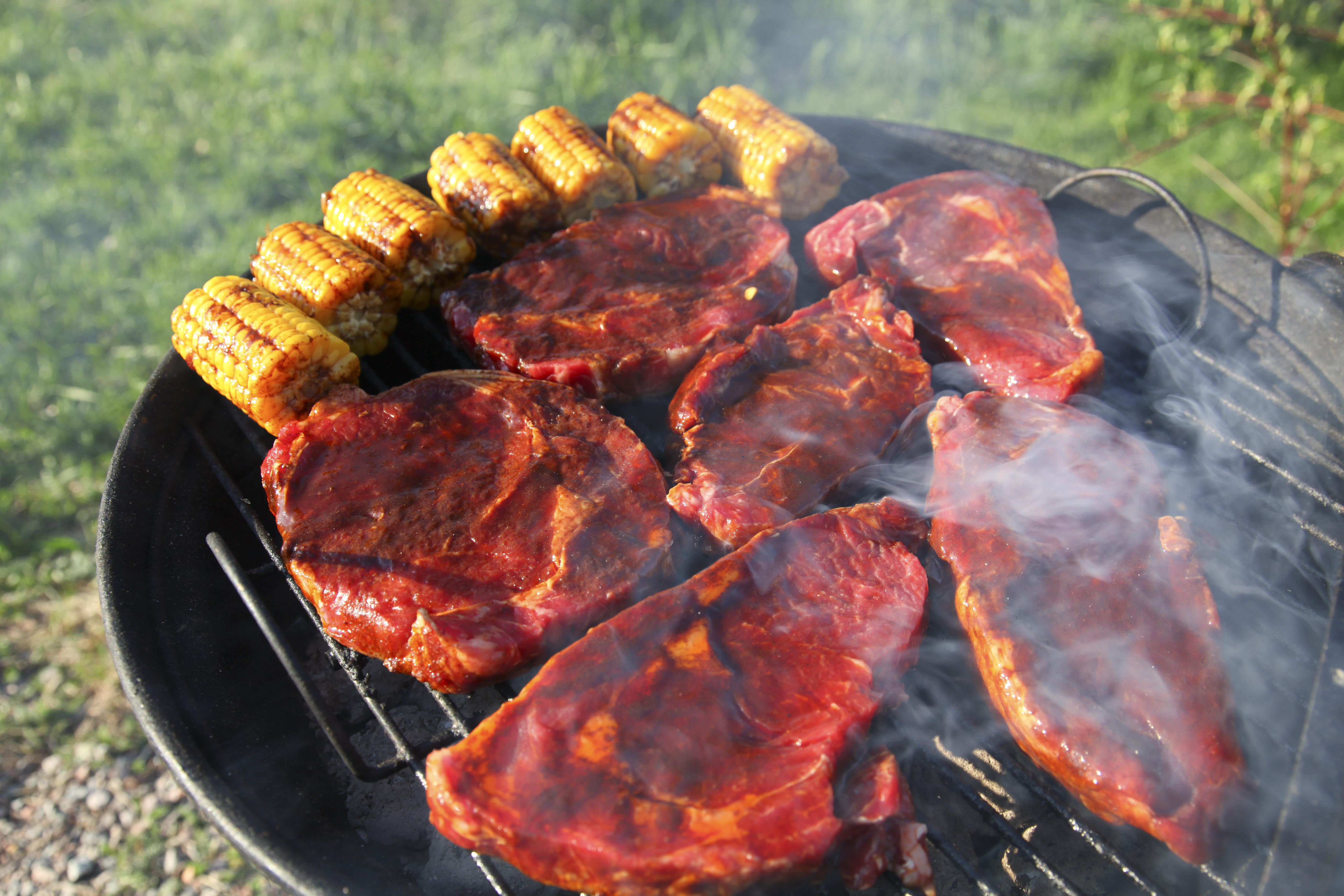 Close detail of meat and cob of corn laying on a barbeque grill with smoke