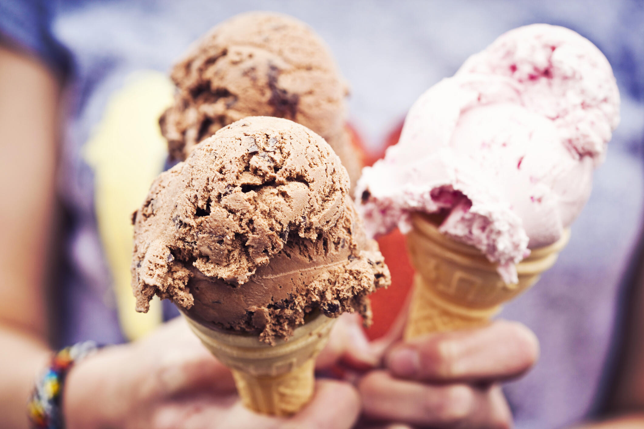 Girl holding three ice cream cones with chocolate and strawberry creams.