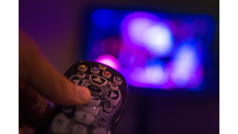 Cropped Image Of Hand Holding Remote Control In Front Of Television Set