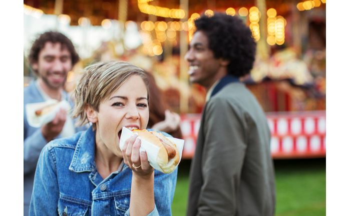 Three young people eating hot-dogs in amusement park