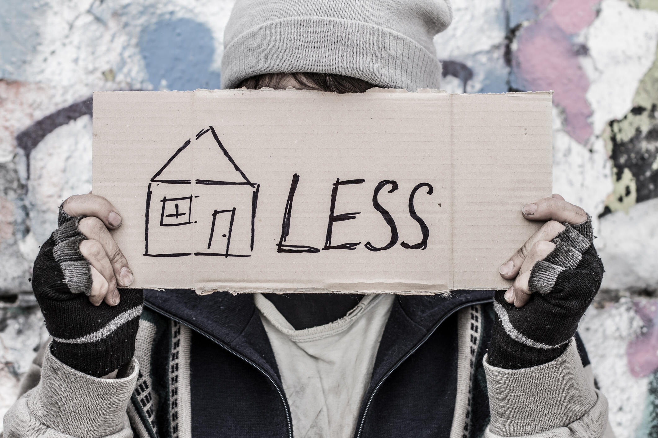 Young homeless man holding cardboard with painted house.