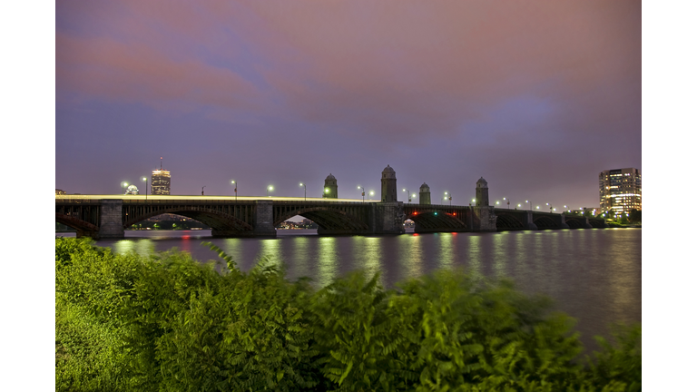 Longfellow bridge stretches across the Charles River at dusk as seen from behind shrubs on the Esplanade. (Credit: Kalim Saliba/ Getty Images /Royalty-Free)