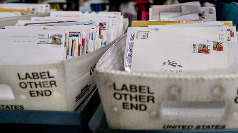 A worker places mail into a tray next to an advanced face cancelling machine at the United States Postal Service (USPS) Suburban processing and distribution center