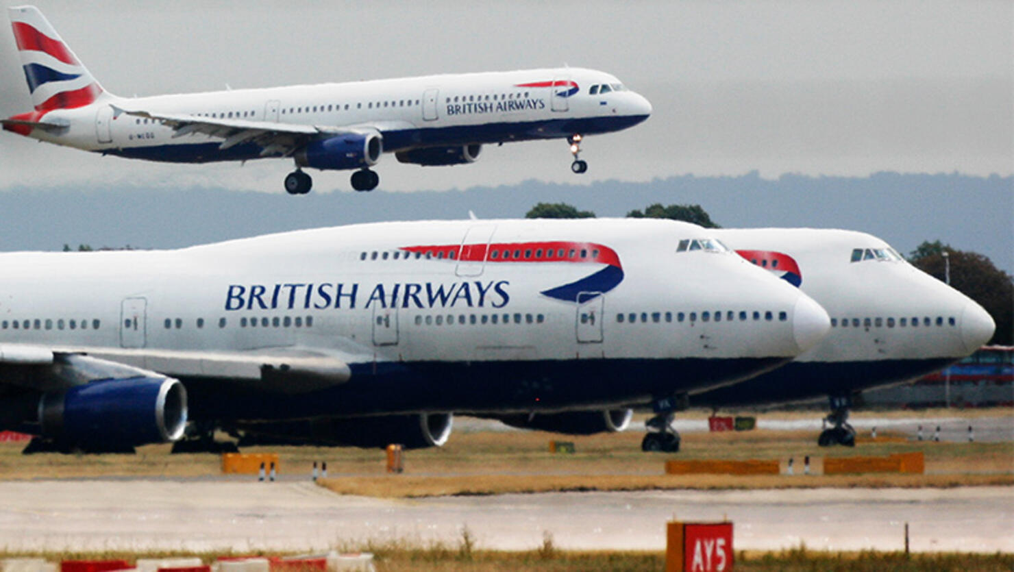 A British Airways plane lands as two other grounded planes sit on the runway at Heathrow Airport, Terminal one