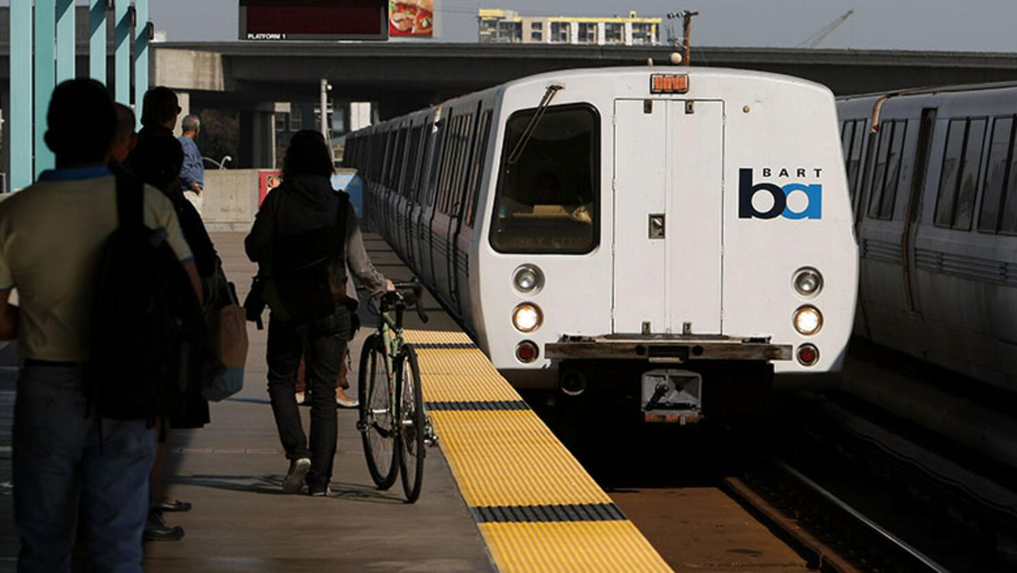 Bay Area Rapid Transit (BART) passengers stand on the platform as a train pulls into the station
