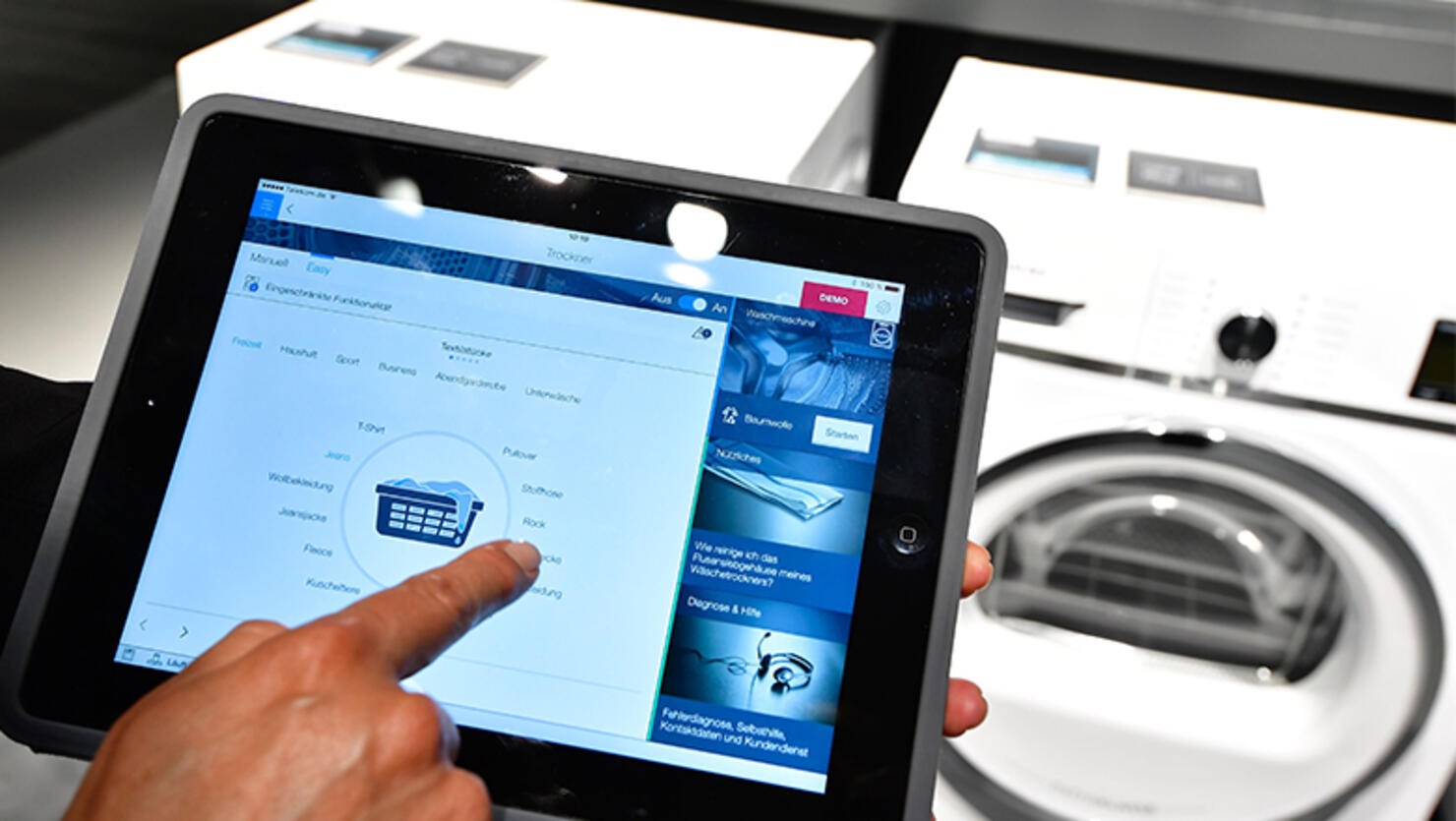 A fair worker uses a tablet to operate a tumble dryer during a demonstration how to operate smart controlled household appliances for 'IQ800' washing and drying machines