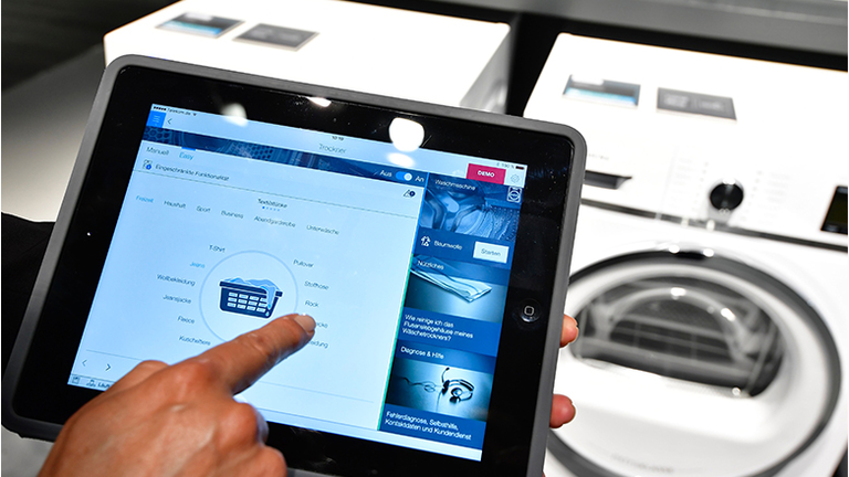 A fair worker uses a tablet to operate a tumble dryer during a demonstration how to operate smart controlled household appliances for 'IQ800' washing and drying machines
