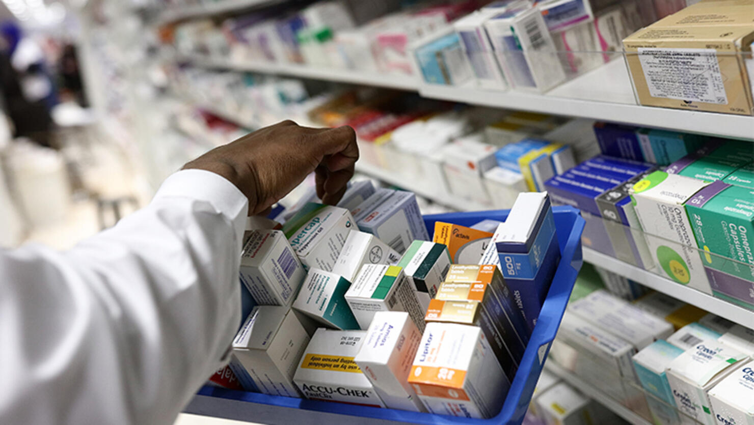 A pharmacist collects packets of boxed medication from the shelves of a pharmacy