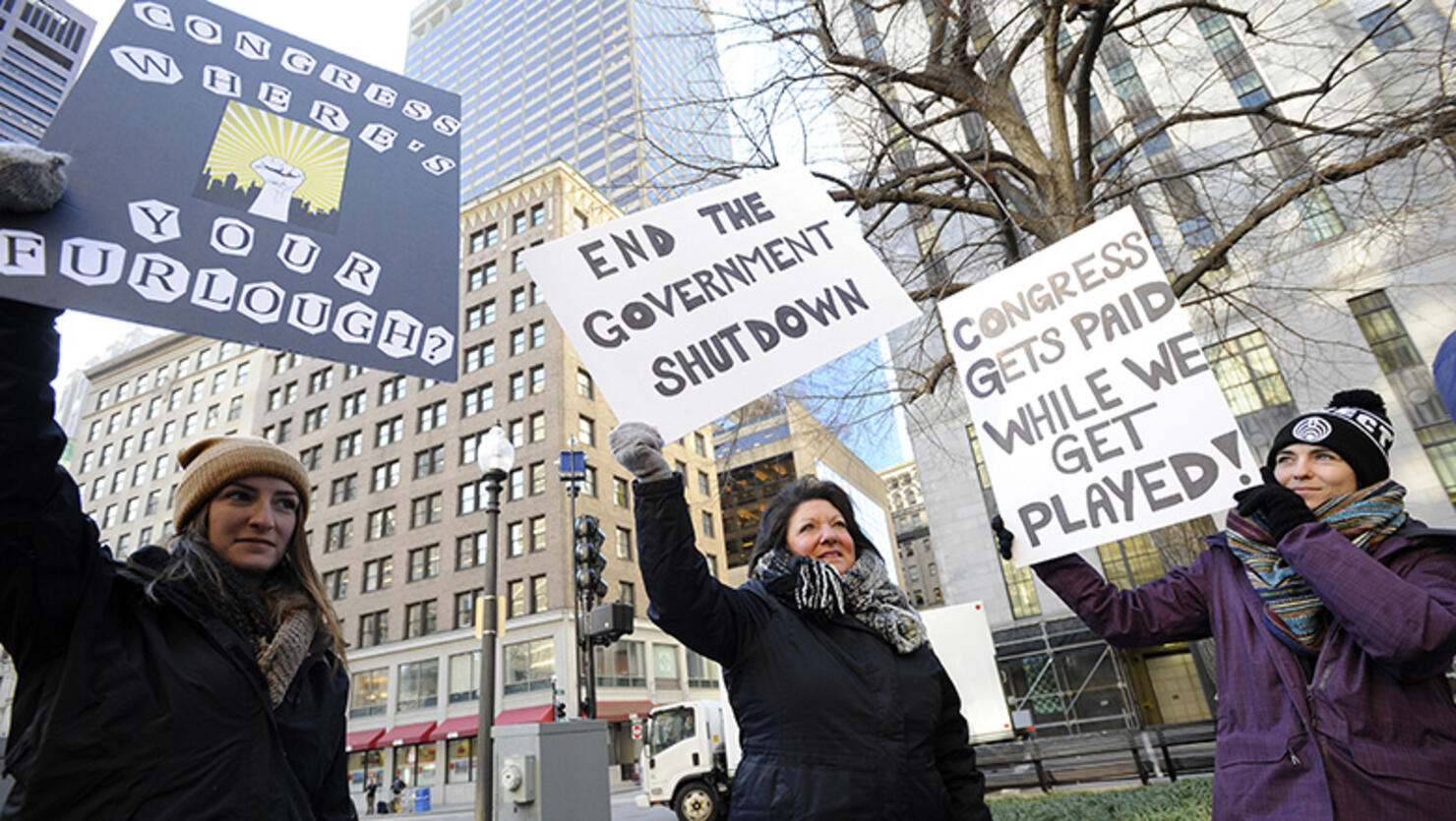 EPA employee Rosanne Sawaya-Obrien (C) holds her sign calling for an end to the government shutdown during a rally and protest by government workers and concerned citizens at Post Office Square near the Federal building, headquarters for the EPA and IRS in Boston