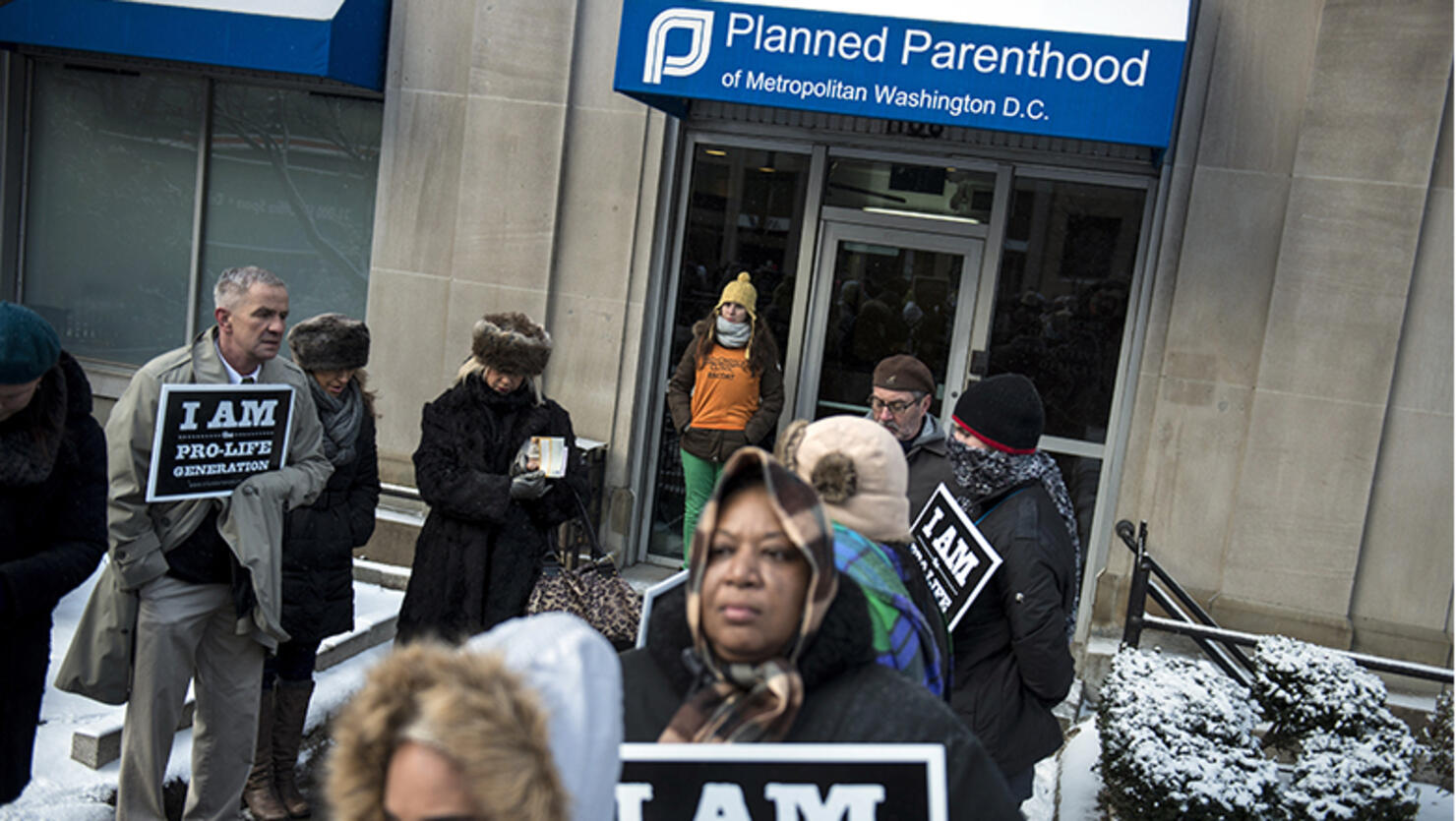 A pro-choice escort waits at the doors of a Planned Parenthood as pro-life activists rally during a protest