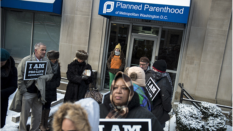 A pro-choice escort waits at the doors of a Planned Parenthood as pro-life activists rally during a protest
