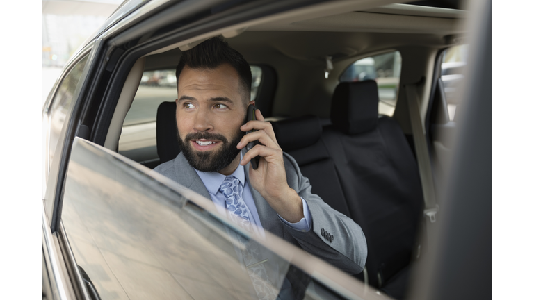 Businessman talking on smart phone in back seat of crowdsourced taxi