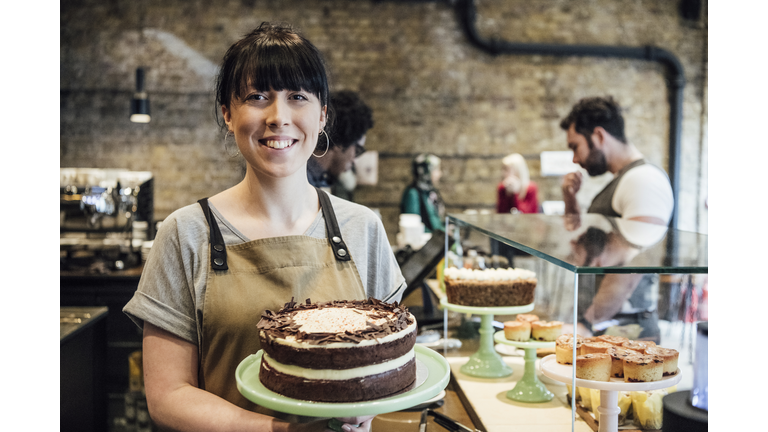 Cheerful young woman holding homemade cake in cafe smiling