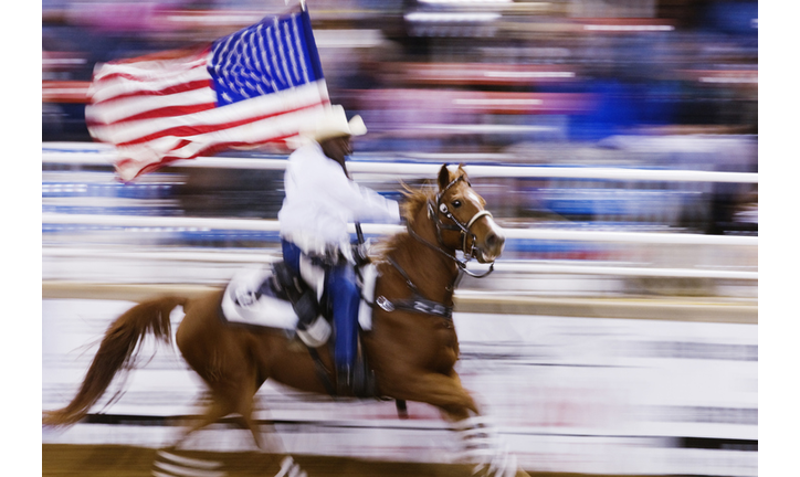 Blurred motion view of cowboy riding horse with American flag in rodeo